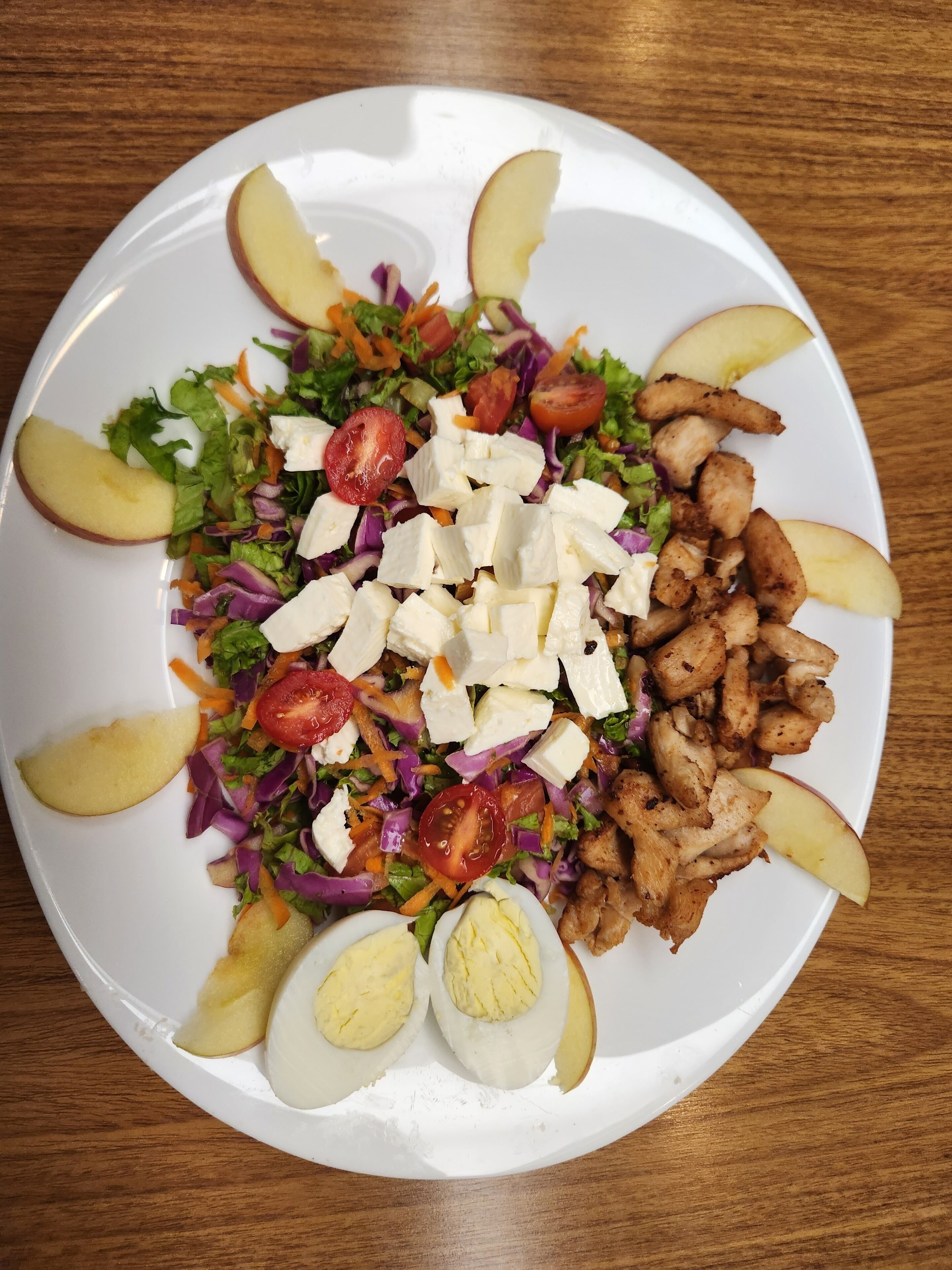 Un plato de comida con ensalada, pollo y rodajas de manzana.