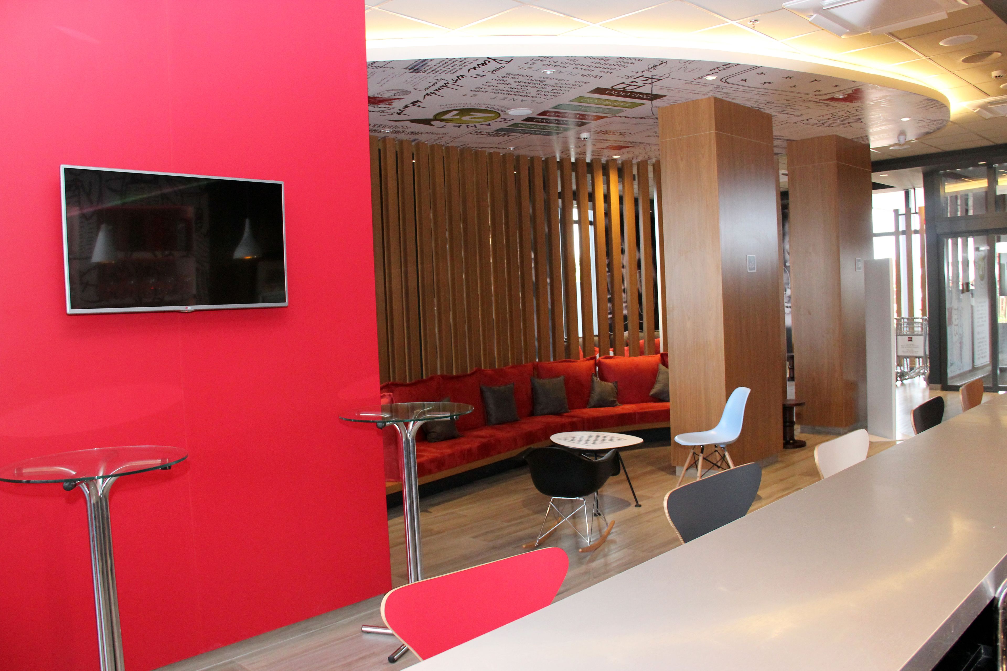 A modern interior with a red wall, a wooden slatted partition, a red sofa with cushions, a white table, and several chairs.