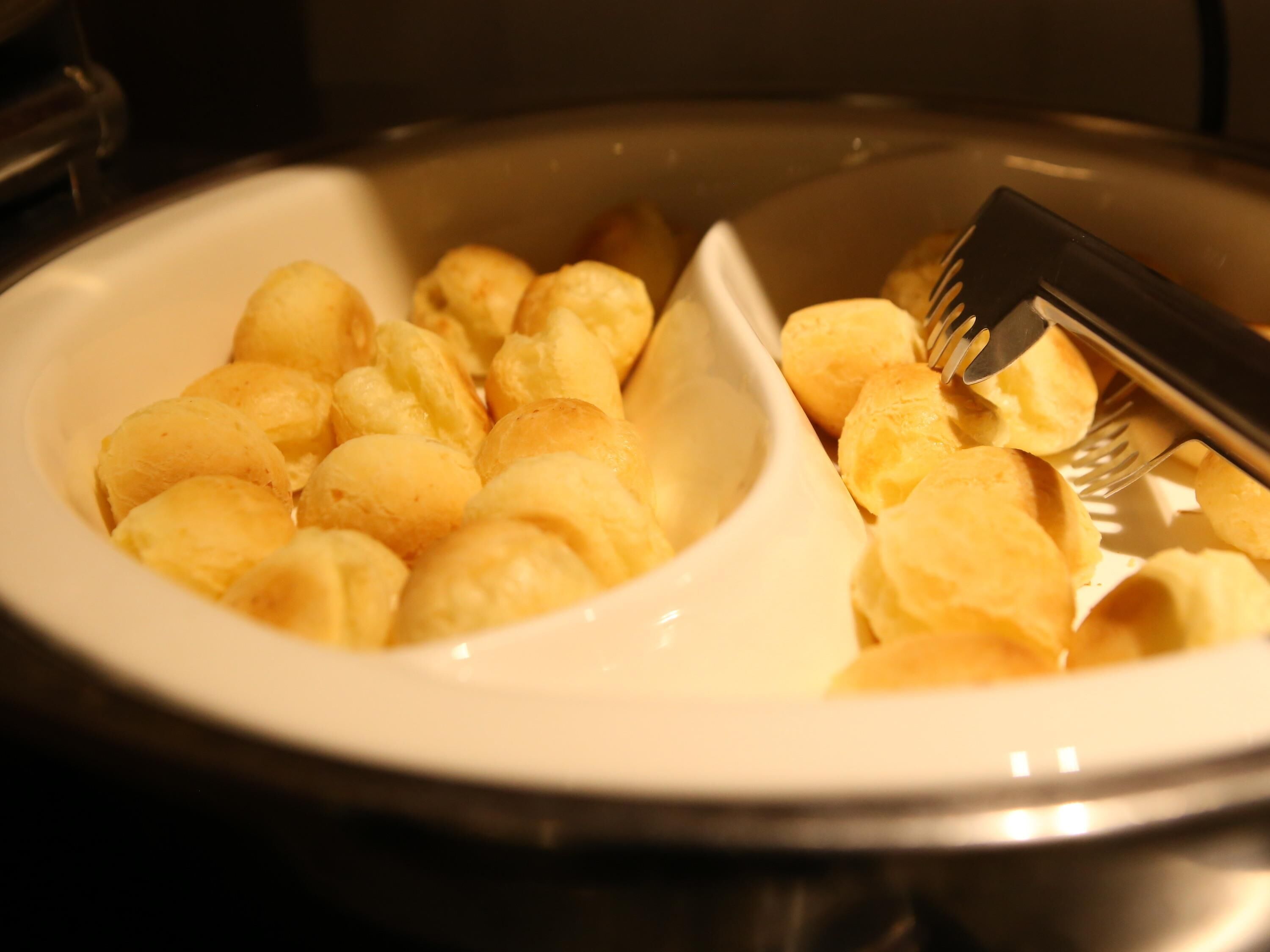 A white bowl containing round, golden-brown pastries, with a fork and knife on the side.
