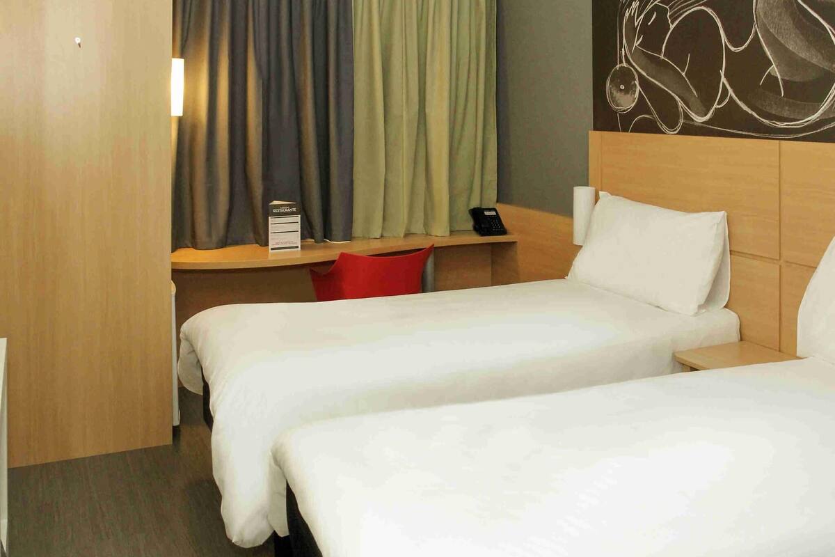 A hotel room with two beds, a desk with a telephone, and a sign indicating a restaurant.
