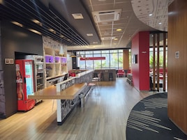 Um café moderno com um balcão comprido, área de estar e uma geladeira Coca-Cola.