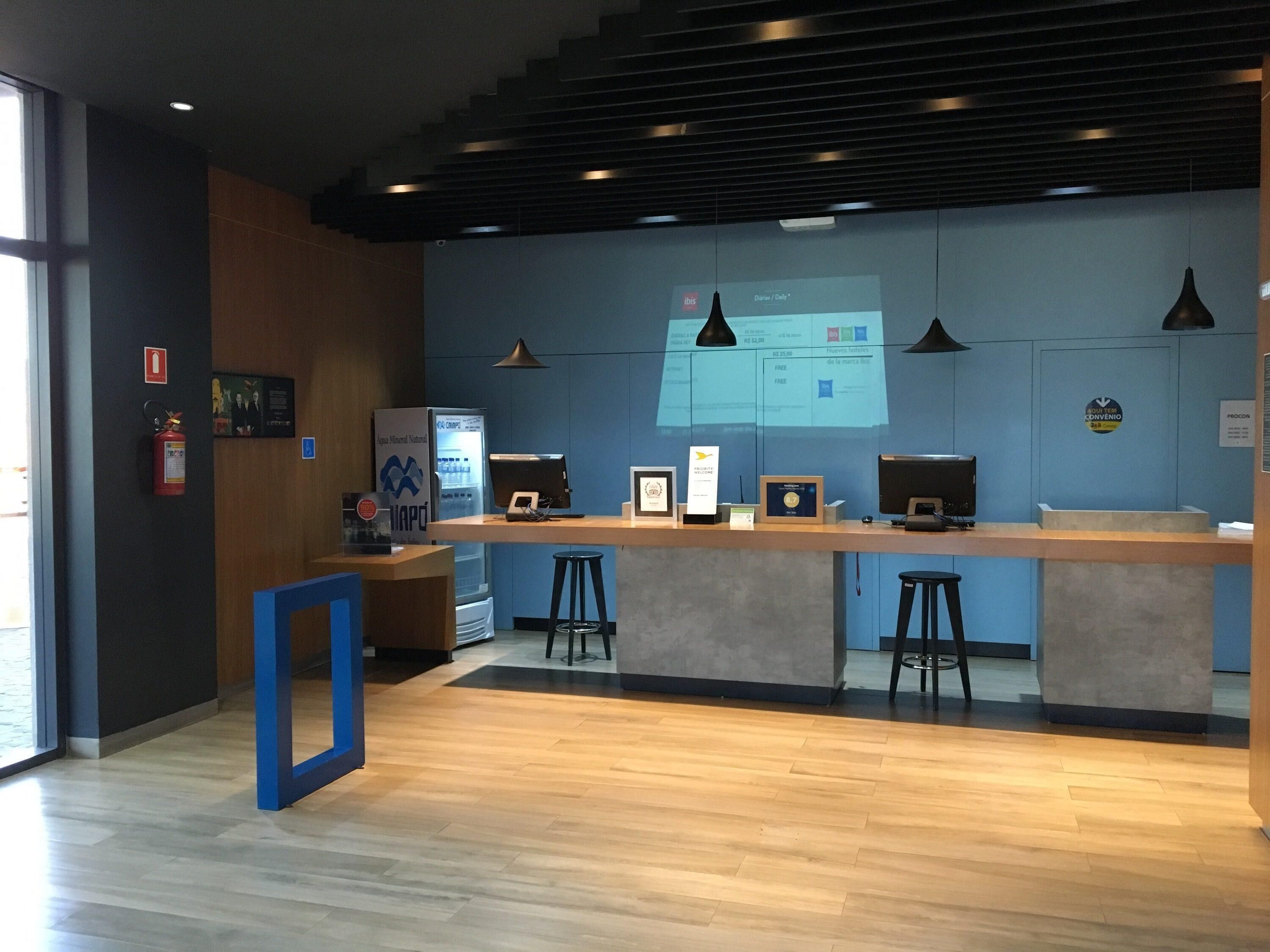 A modern reception desk with a digital screen, bar stools, and a fire extinguisher.