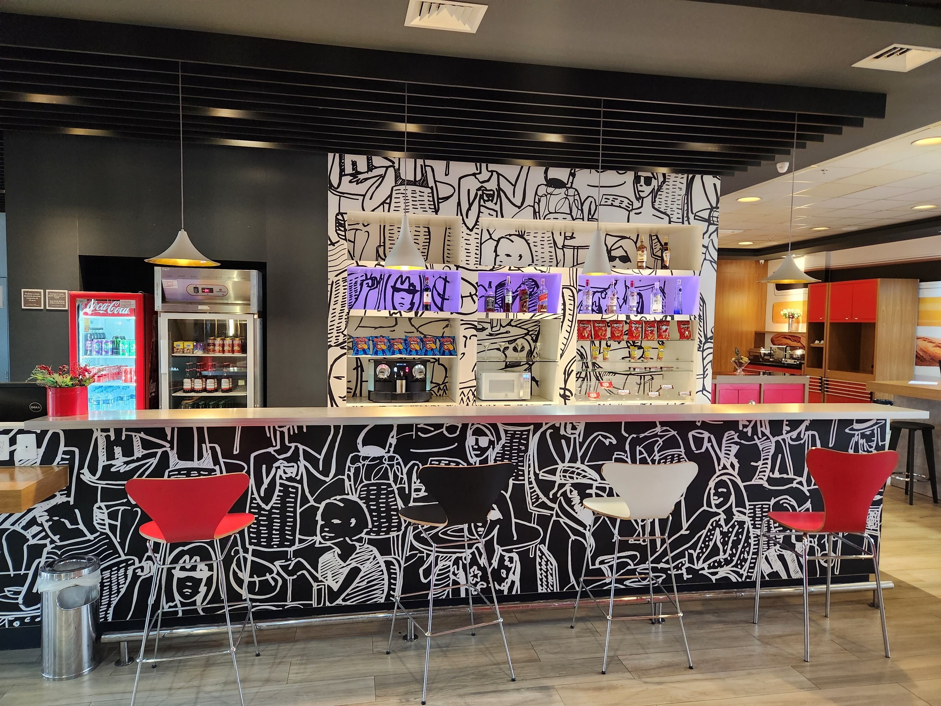 A bar area with a counter, shelves with snacks, a Coca-Cola refrigerator, and red chairs.