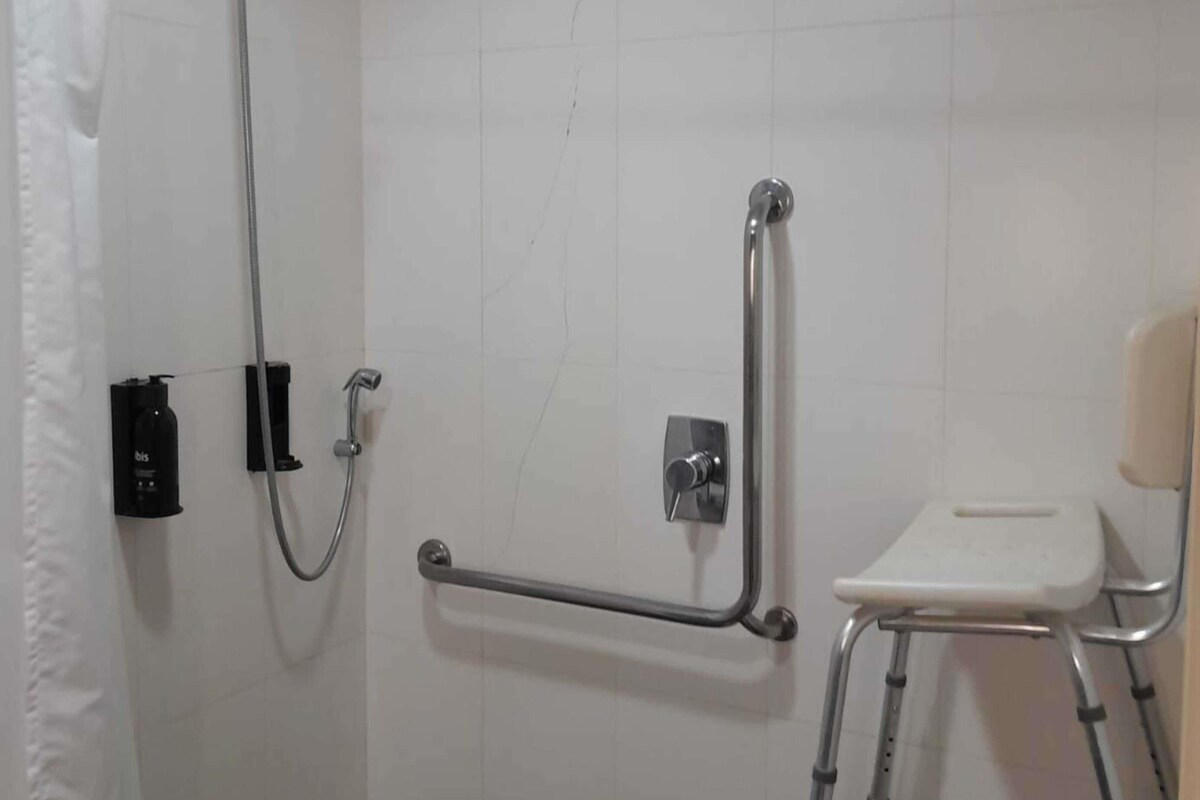 A bathroom with a shower, grab bar, and a wheelchair-accessible bench.