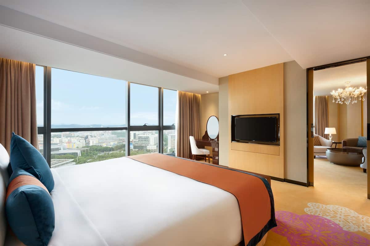 Quarto de hotel com uma cama grande, uma mesa com cadeira, uma televisão e vista para a cidade.
