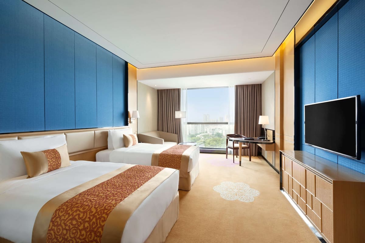 Quarto de hotel com duas camas, uma escrivaninha, televisão e vista para a cidade.