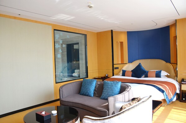 A hotel room with a large bed, a sofa, a small table, and a large window.
