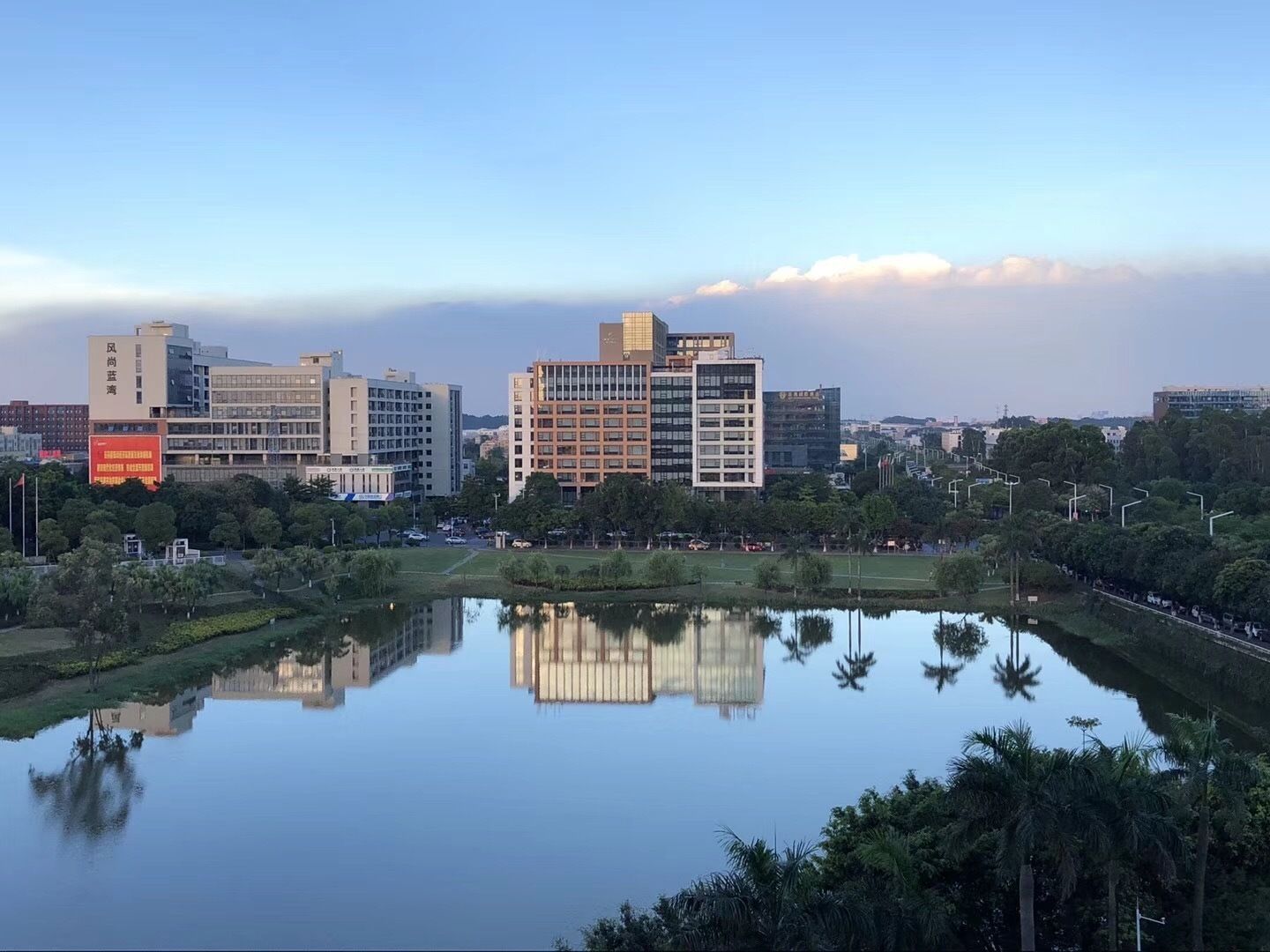 A cityscape with modern buildings, a calm lake reflecting the structures, and a clear sky.