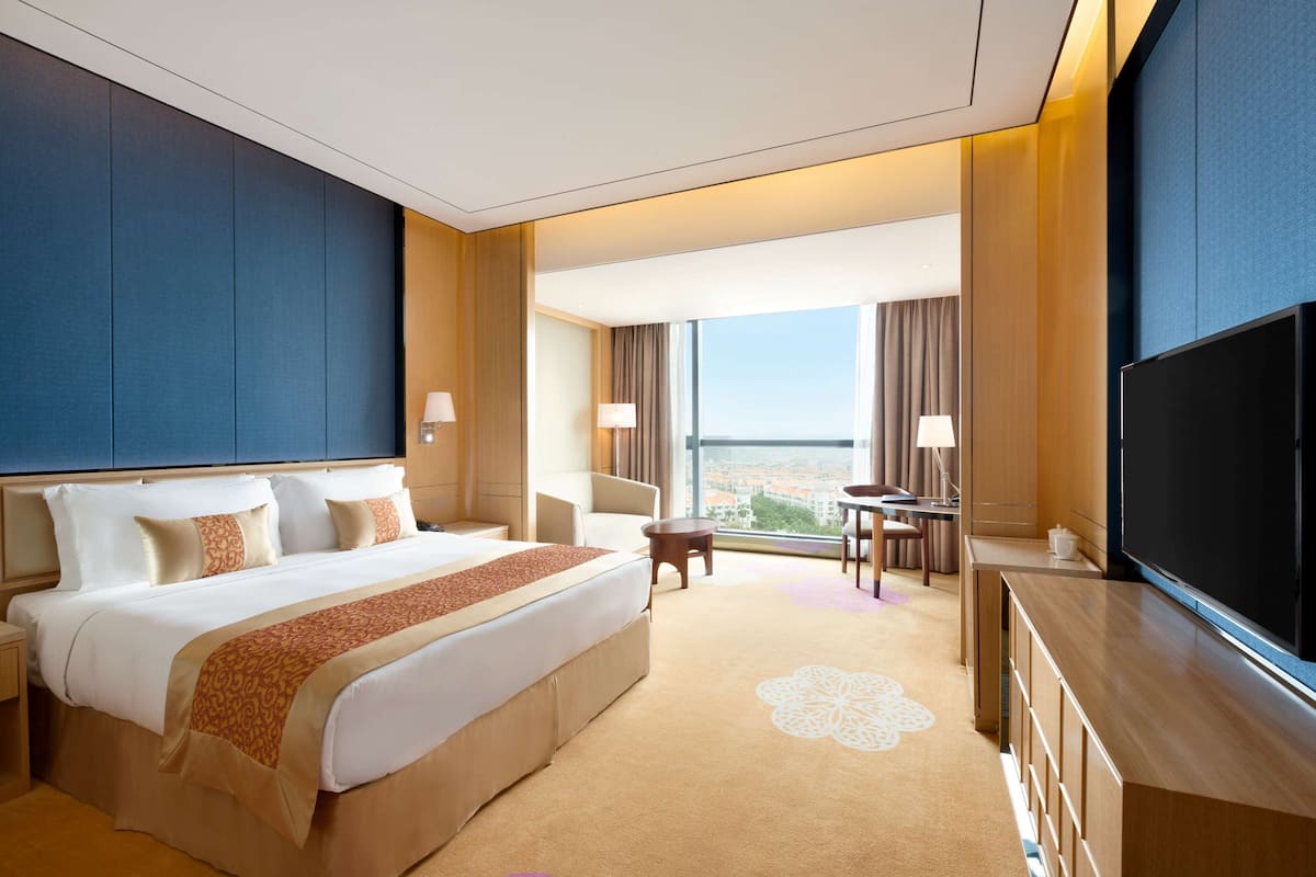 Quarto de hotel com uma cama grande, televisão, escrivaninha e vista para a cidade.