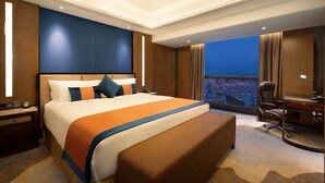 A hotel room with a large bed, a desk, and a view of a cityscape. - Ramada Foshan Nanhai (Foshan)