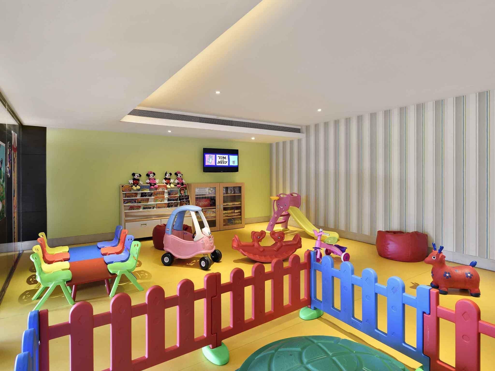 Espaço infantil com brinquedos coloridos e uma tela de televisão exibindo 'TOM Jolly'.
