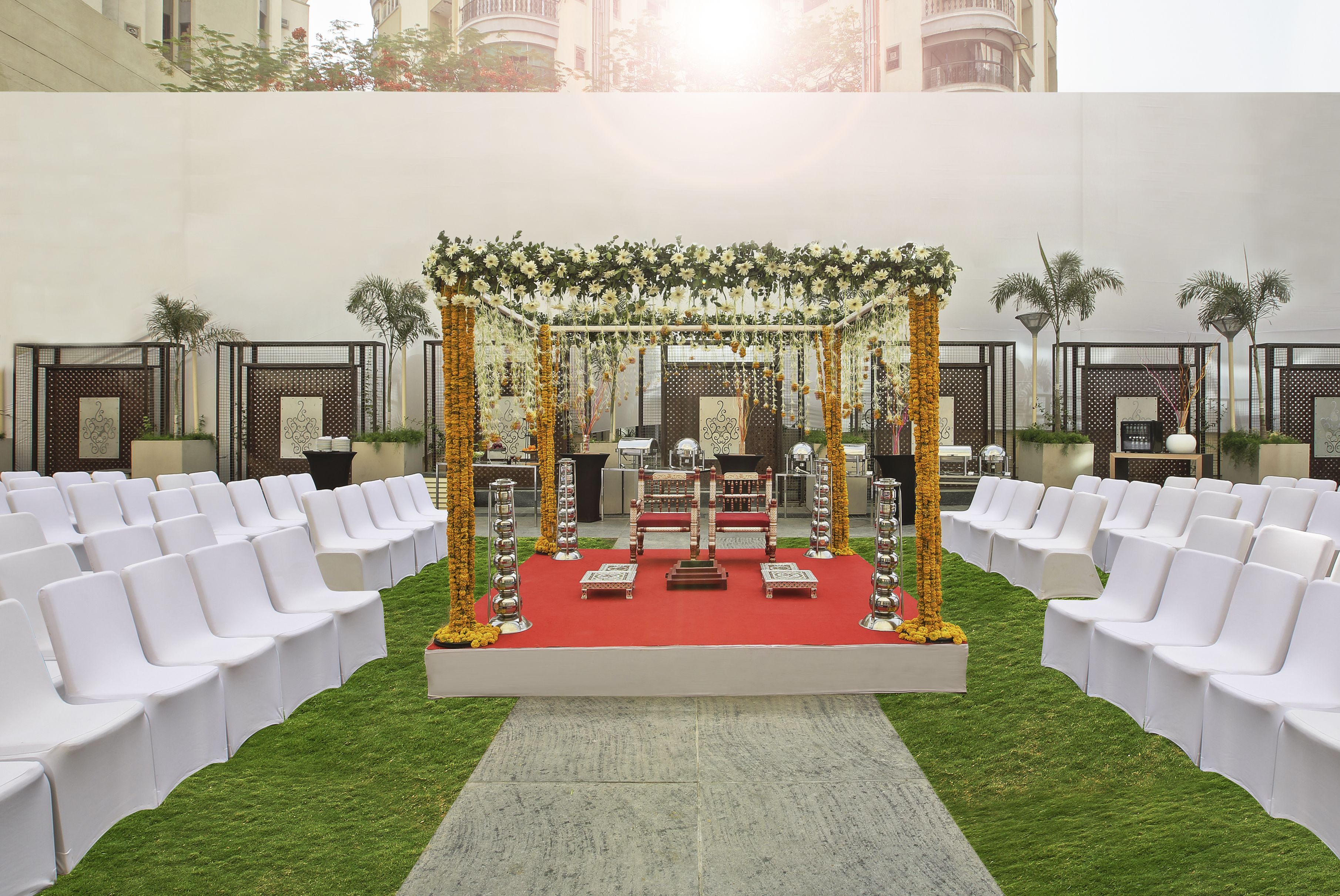 Montaje para una boda al aire libre, con alfombra roja, sillas blancas y un altar decorado.