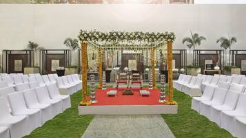 Montaje para una boda al aire libre, con alfombra roja, sillas blancas y un altar decorado.