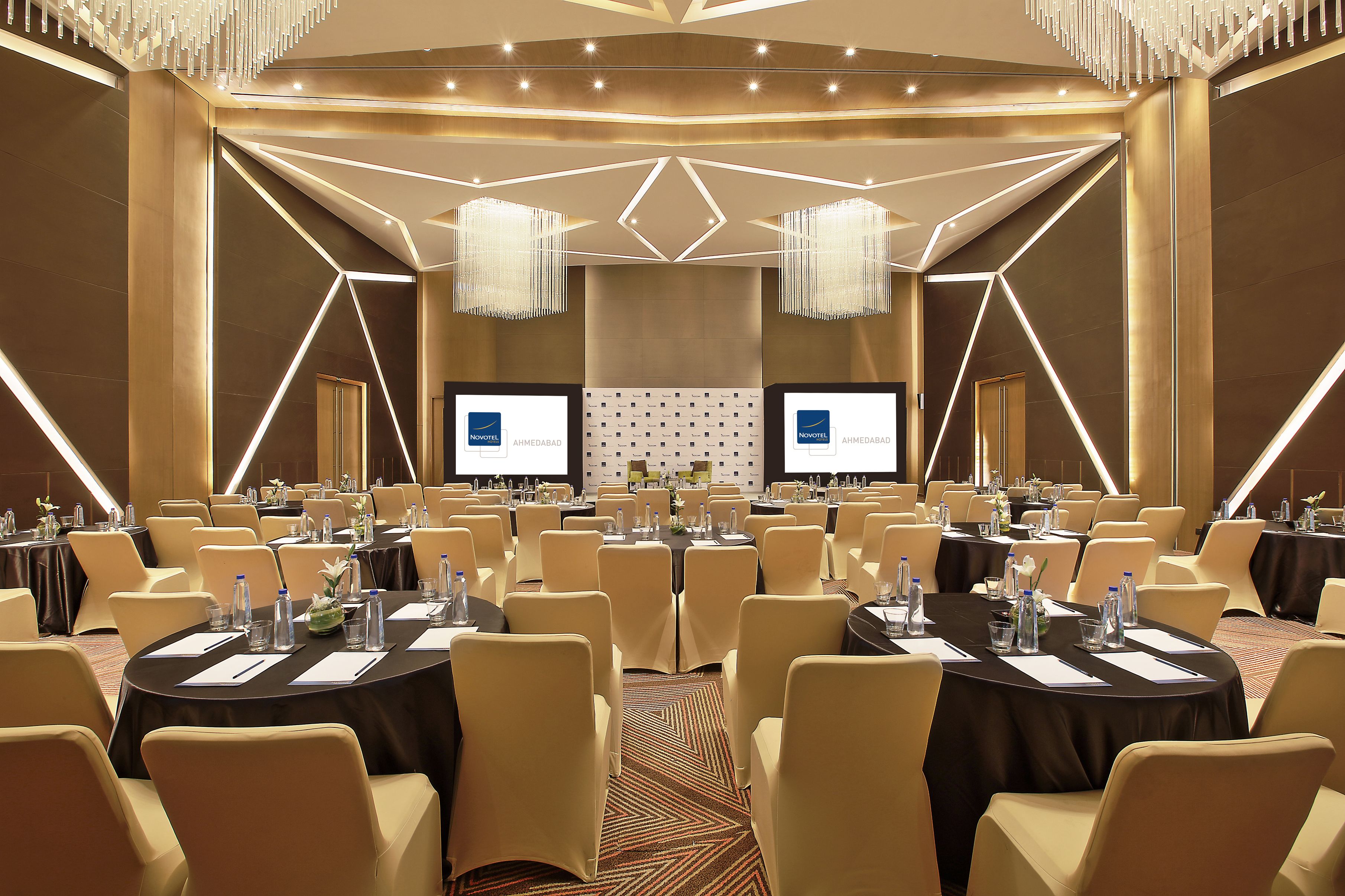 Une salle de conférence équipée de tables rondes, de chaises et d’une scène avec des écrans.