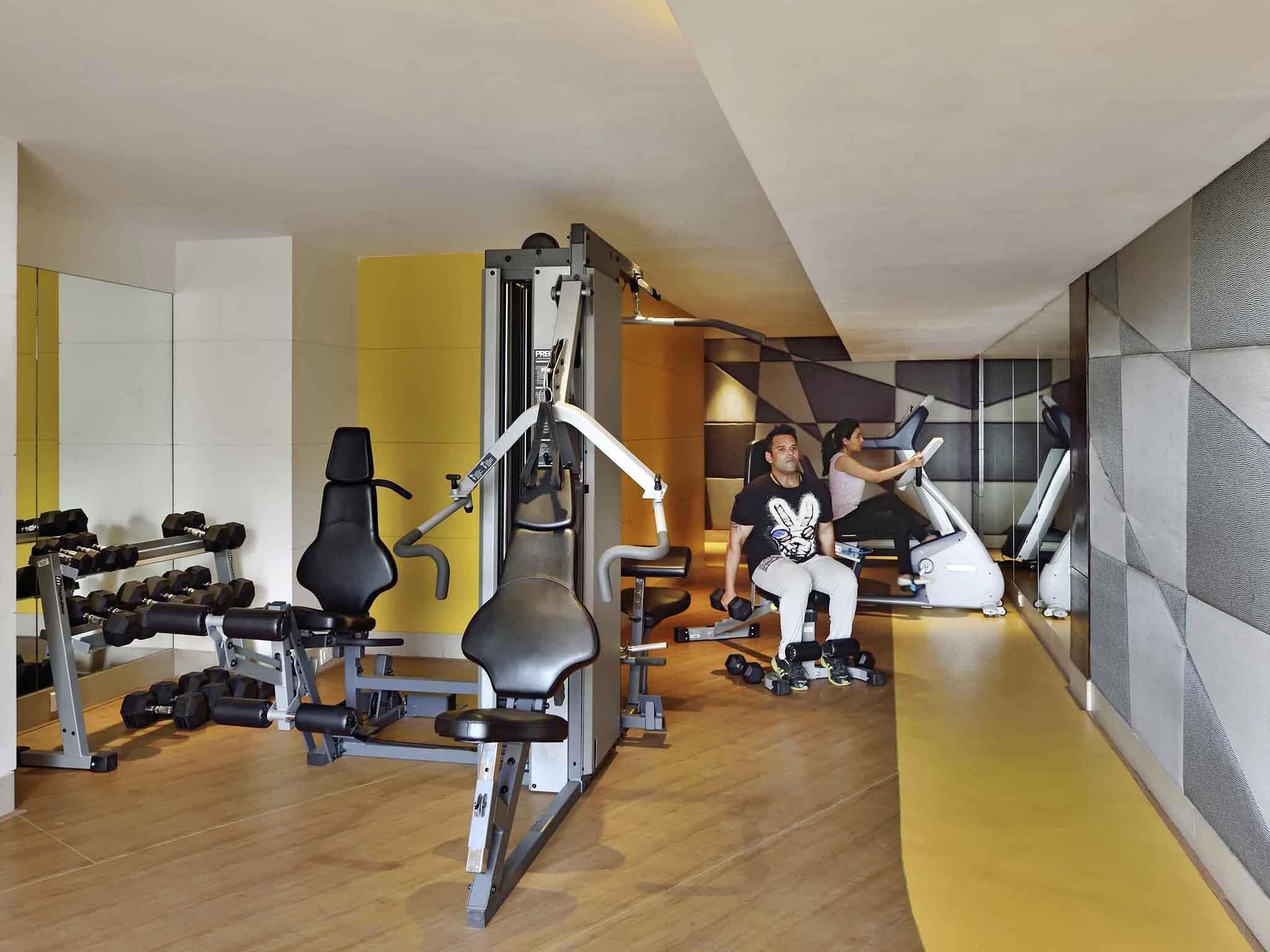 A modern gym with various exercise equipment, including a bench press, dumbbells, and a treadmill.