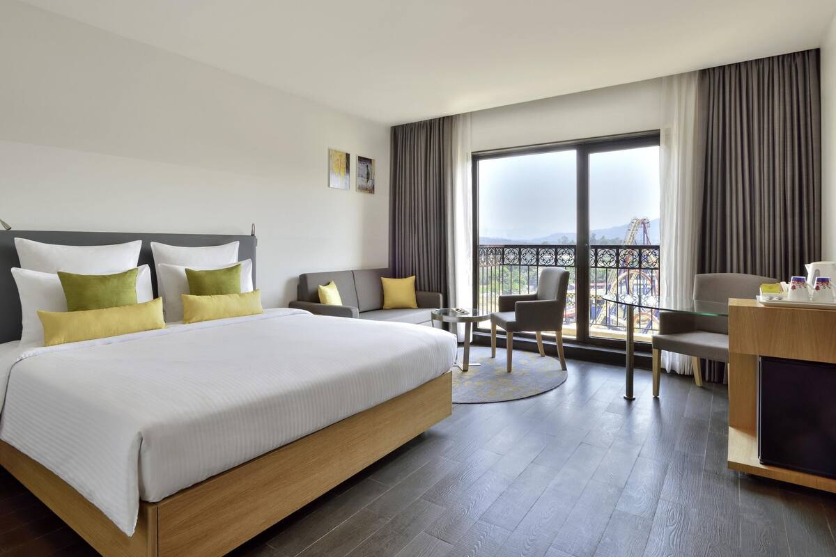 A hotel room with a bed, a desk, a chair, and a balcony with a view.
