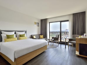 A hotel room with a bed, a desk, a chair, and a balcony with a view.