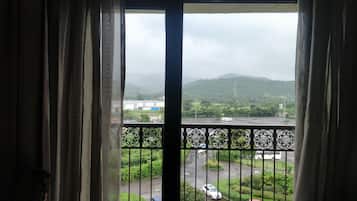 Vista desde una ventana con cortinas, que da a un estacionamiento con varios coches y un paisaje verde con colinas al fondo.