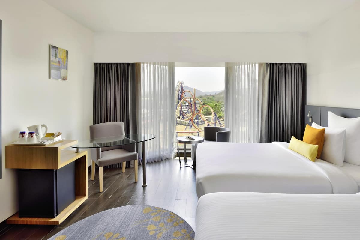A hotel room with a bed, a desk with a chair, a small table, and a view of an amusement park.