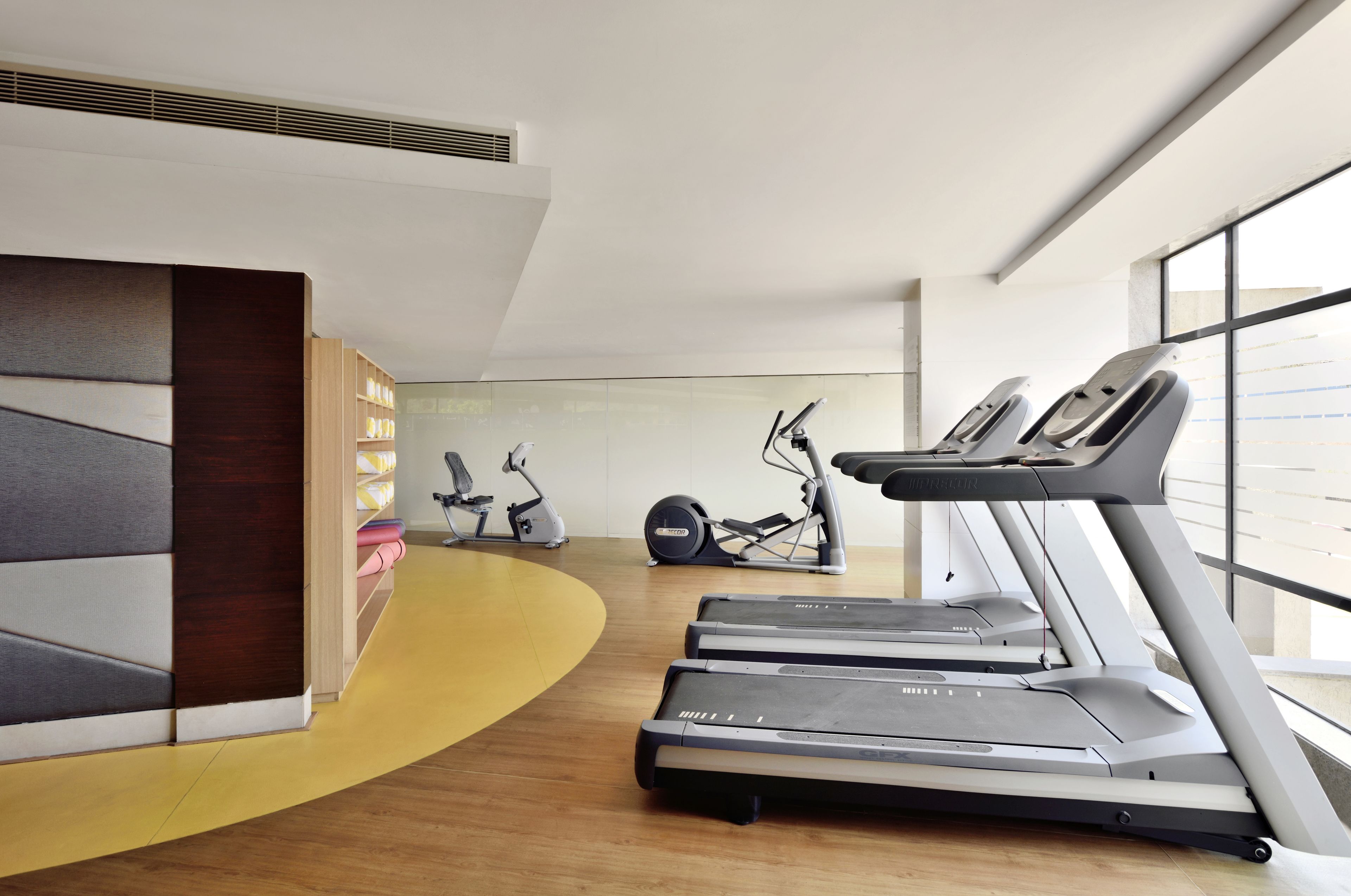 A modern gym with treadmills, stationary bikes, and a curved wooden floor.