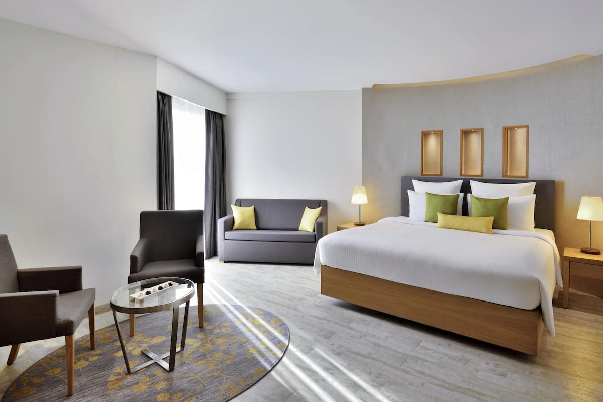 A hotel room with a bed, two chairs, a small table, and a nightstand with lamps.