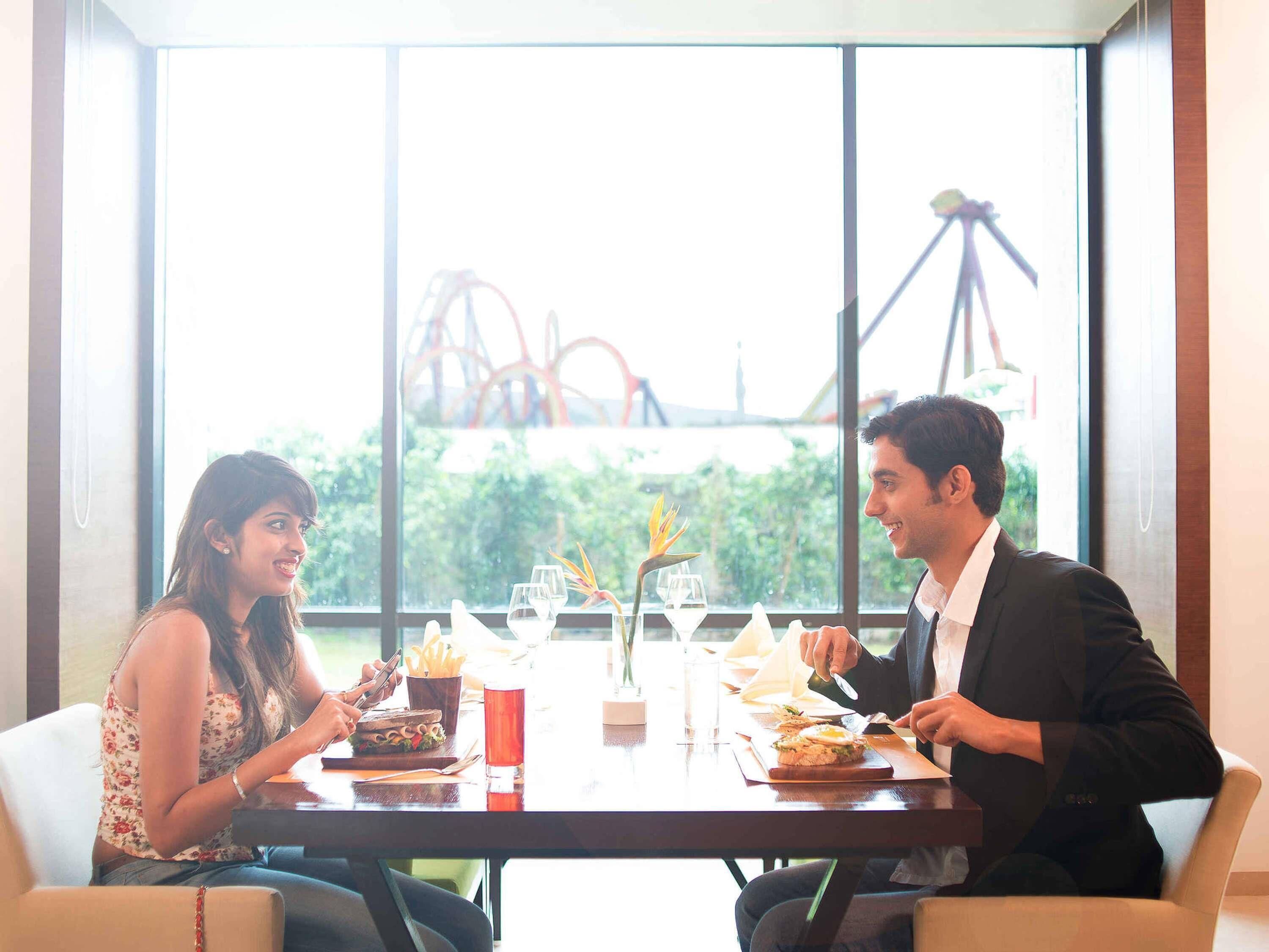 A dining table with food and drinks, a window with a view of greenery and a roller coaster.