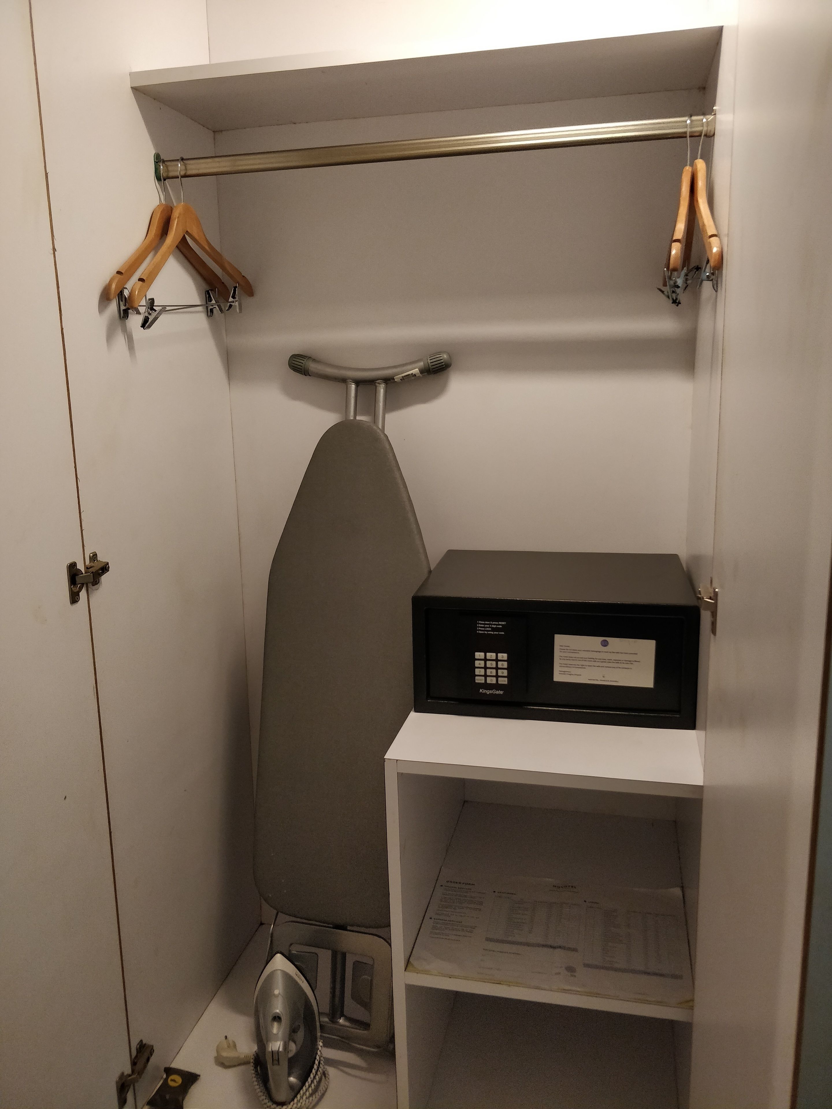 Una habitación pequeña con un armario blanco, una tabla de planchar y un planchador compacto.