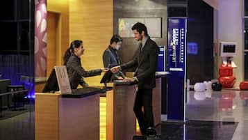 A hotel reception area with a wooden reception desk, a digital screen, and a Novotel logo.