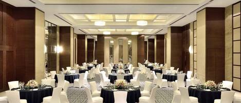 A banquet hall with round tables, white chairs, and chandeliers.