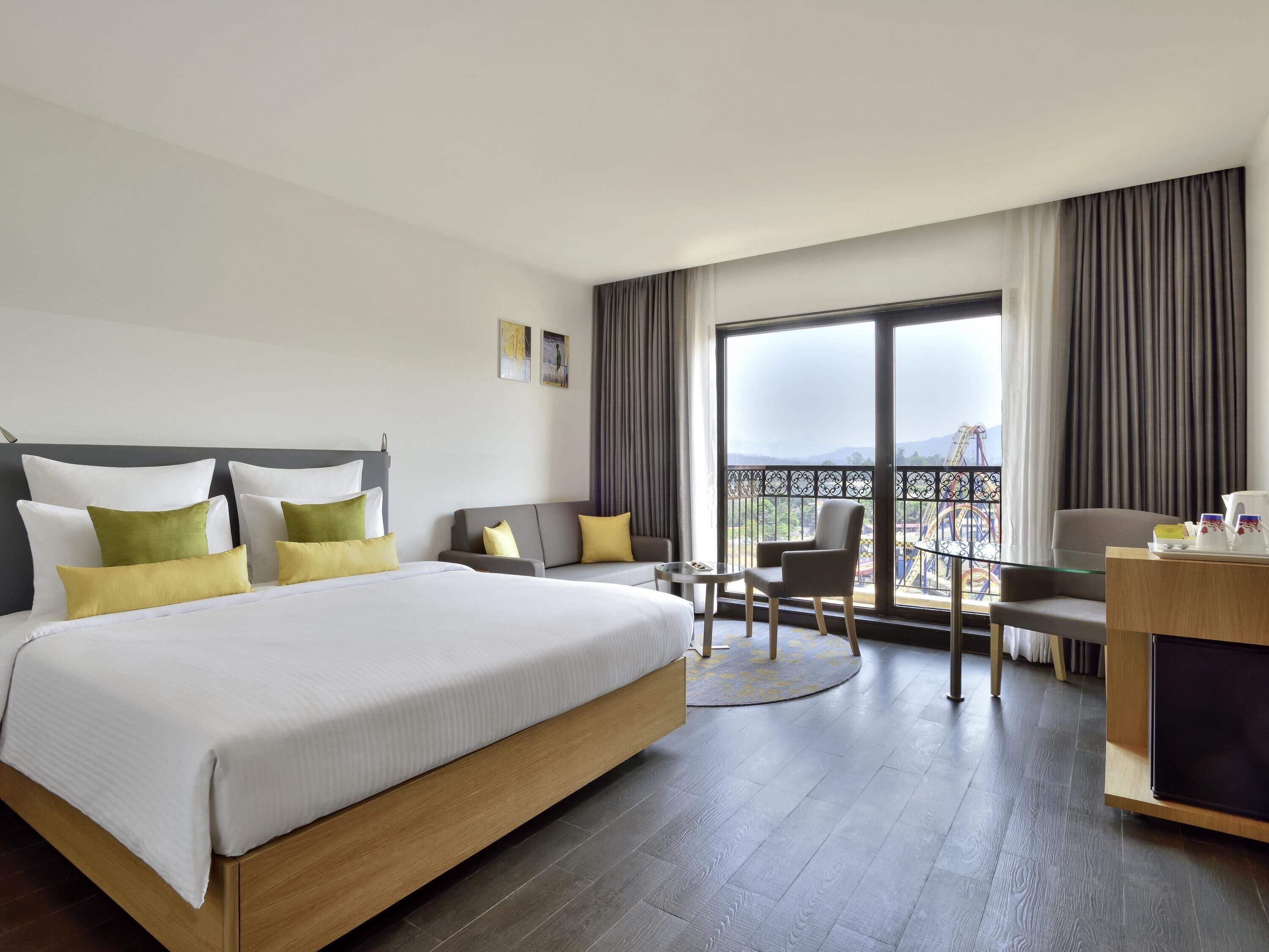 A hotel room with a large bed, a desk, a chair, and a balcony with a view.