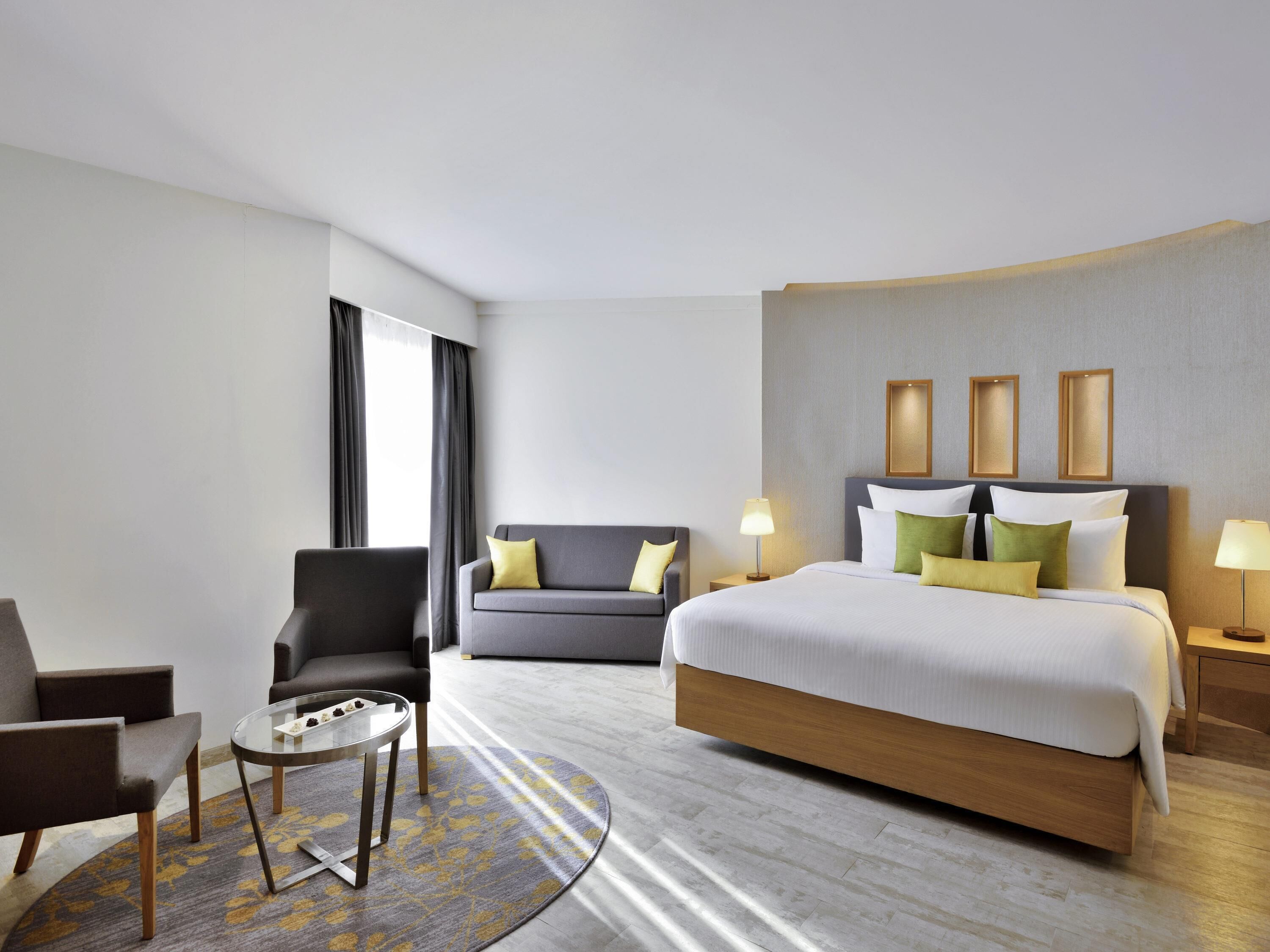 A hotel room with a bed, two chairs, a small table, and a nightstand with lamps.