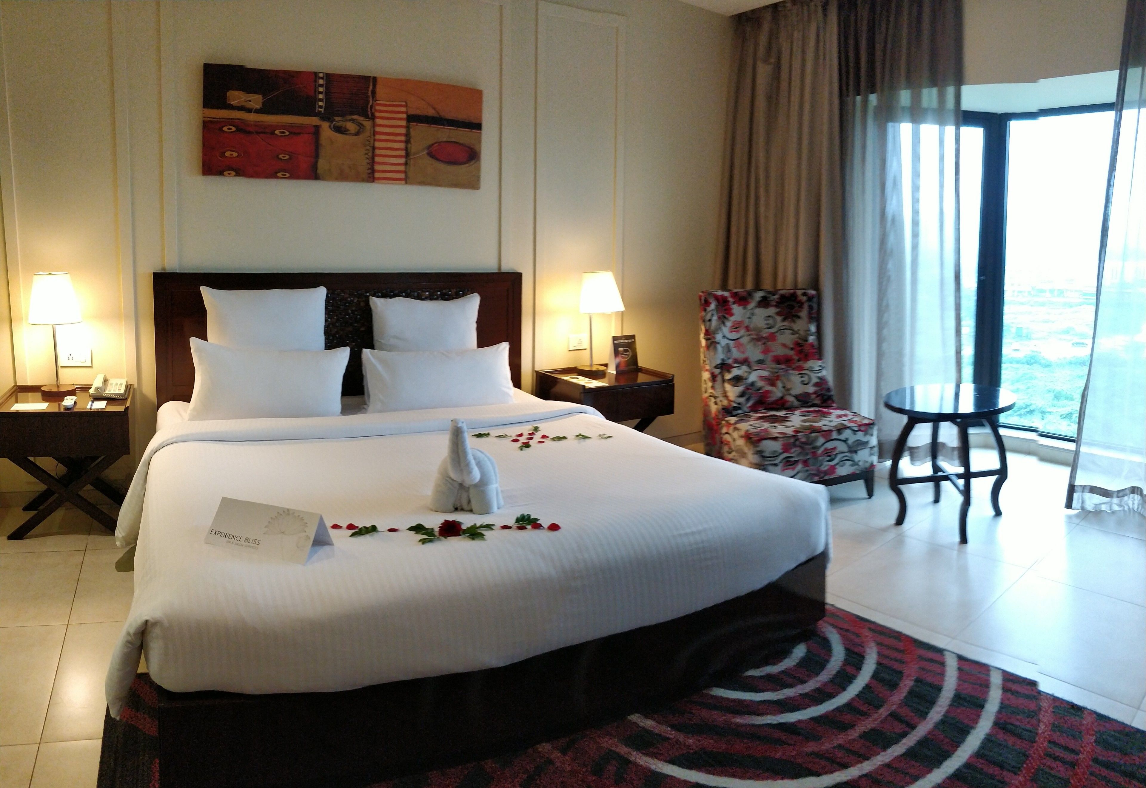 A hotel room with a large bed, two bedside tables, a chair, and a view of the outdoors.