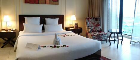 A hotel room with a large bed, two bedside tables, a chair, and a view of the outdoors.