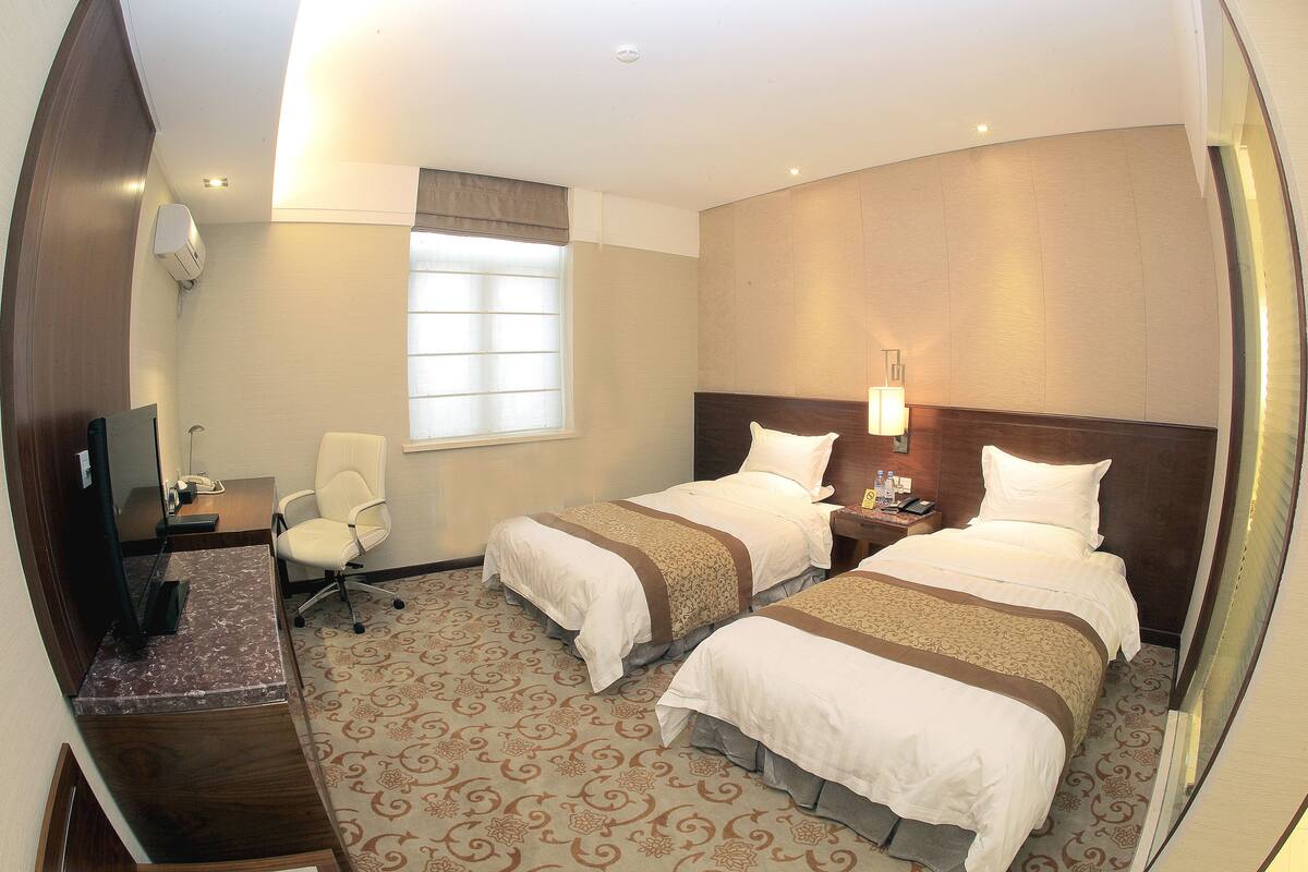 A hotel room with two beds, a desk with a computer, a chair, and a window with blinds.