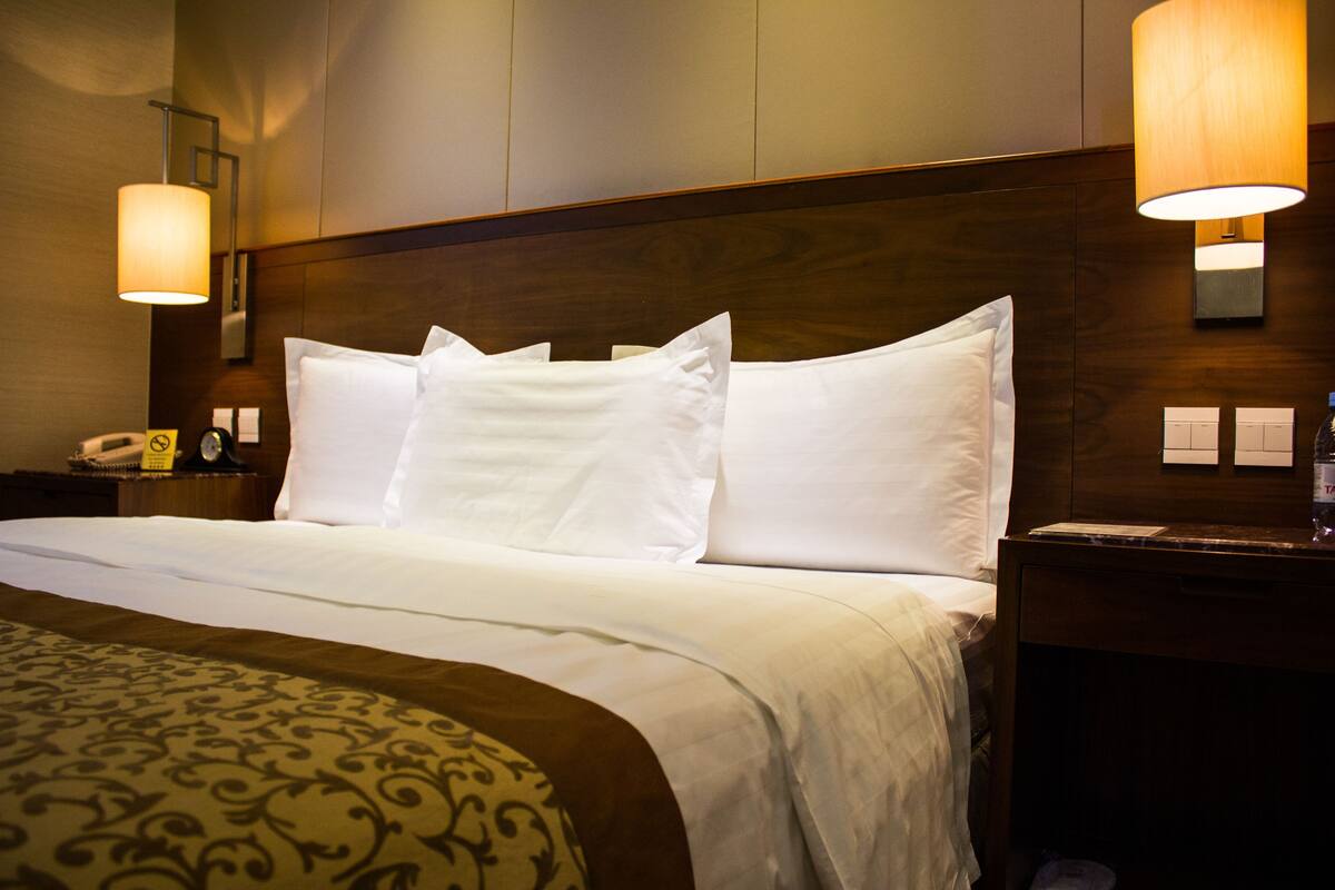 A hotel room with a large bed, two bedside lamps, a nightstand with a phone, and a wooden headboard.