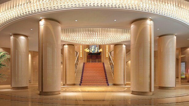 Eine beeindruckende Lobby mit einer zentralen Treppe, großen Säulen und einer verzierten Decke.