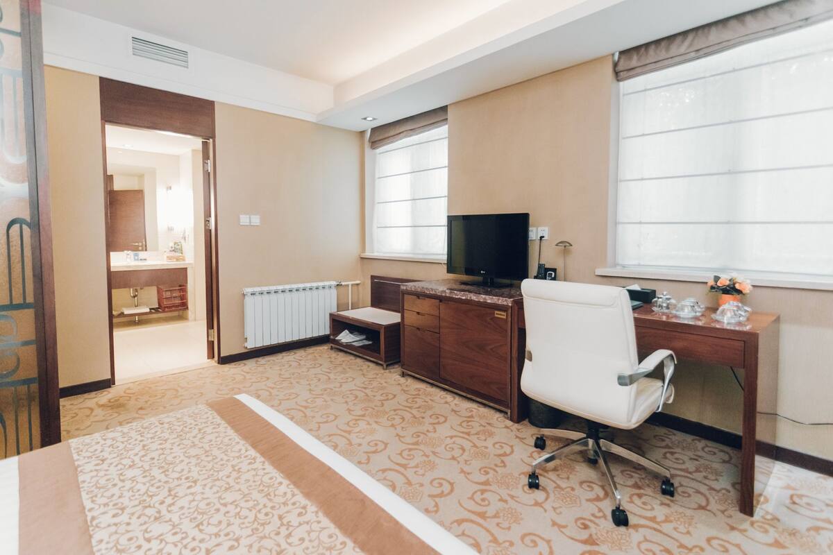 A hotel room with a bed, a desk with a computer, a TV, and a window with curtains.