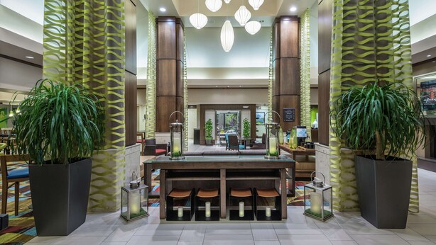 A lobby with a reception desk, potted plants, and hanging pendant lights. - Hilton Garden Inn San Antonio At The Rim (San Antonio)