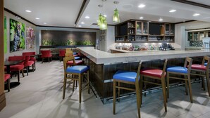 A modern bar area with a counter, bar stools, and a variety of bottles and glasses. - Hilton Garden Inn San Antonio At The Rim (San Antonio)