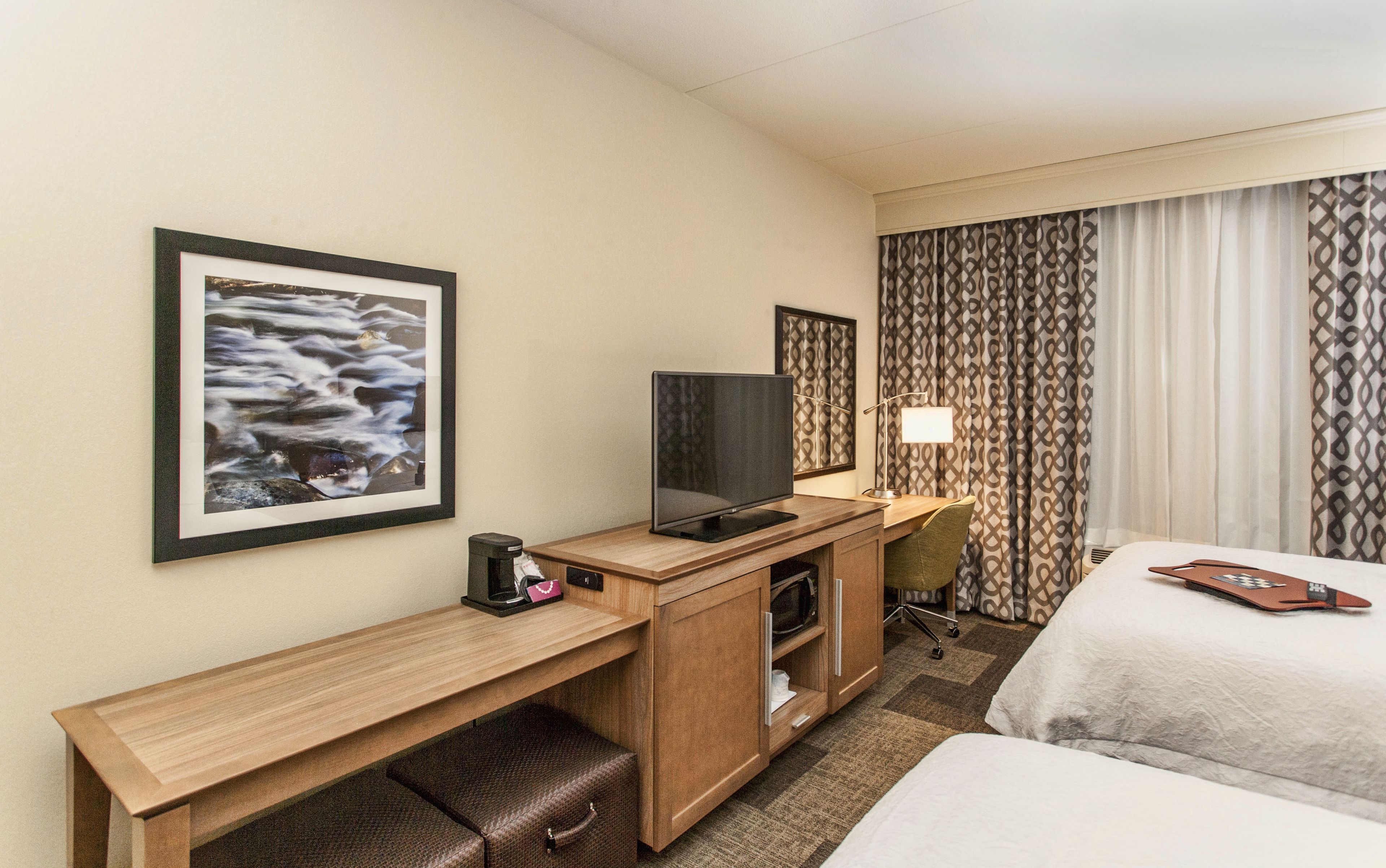 Een hotelkamer met een bed, een bureau met een televisie, een lamp en een foto aan de muur.