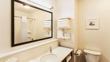 A bathroom with a large mirror, a sink, a toilet, and shelves with towels.