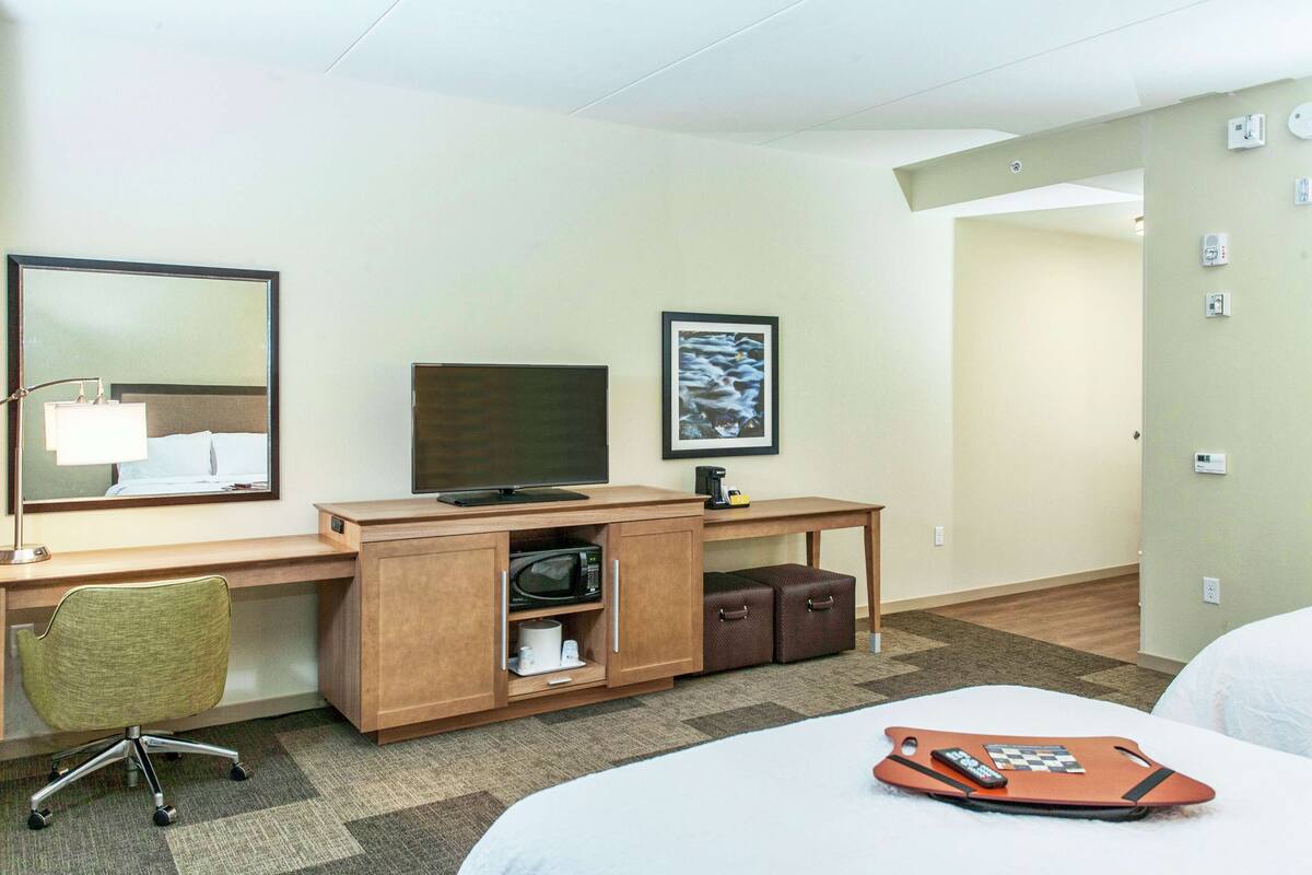 A hotel room with a bed, a desk with a computer, a chair, a TV, a microwave, and a small cabinet.