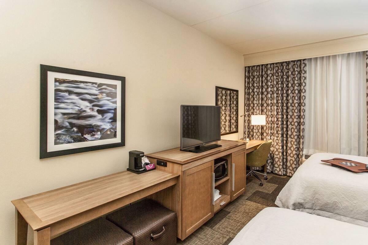 A hotel room with a bed, a desk with a computer, a TV, a lamp, and a picture on the wall.