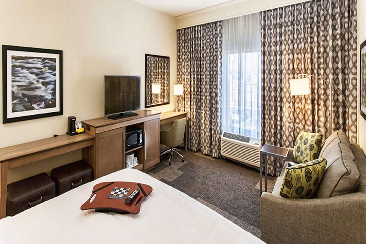 A hotel room with a bed, a desk with a TV, a chair, a couch, and curtains.