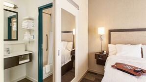 A hotel room with a bed, a nightstand, a lamp, a bathroom with a sink, and a mirror. - Hampton Inn Hibbing (Hibbing)
