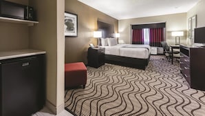 A hotel room with a bed, desk, chair, TV, and a minibar. - La Quinta Inn & Suites by Wyndham Collinsville - St. Louis (Collinsville)