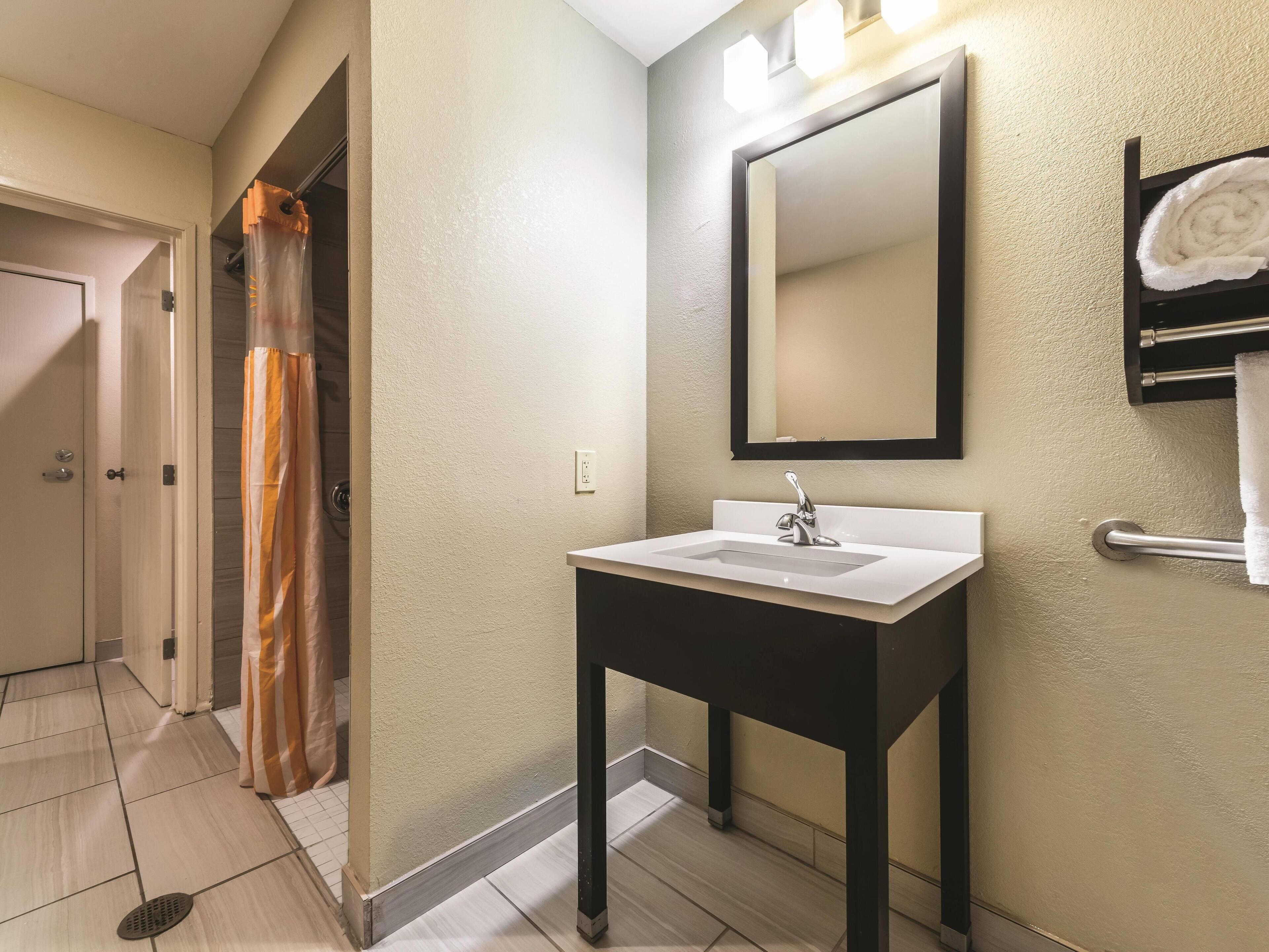 Un baño con lavamanos blanco, tocador negro, espejo y perchero.