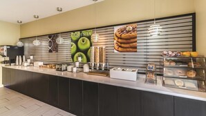 A counter with a coffee machine, condiment dispensers, and a display case with pastries. - La Quinta Inn & Suites by Wyndham Collinsville - St. Louis (Collinsville)