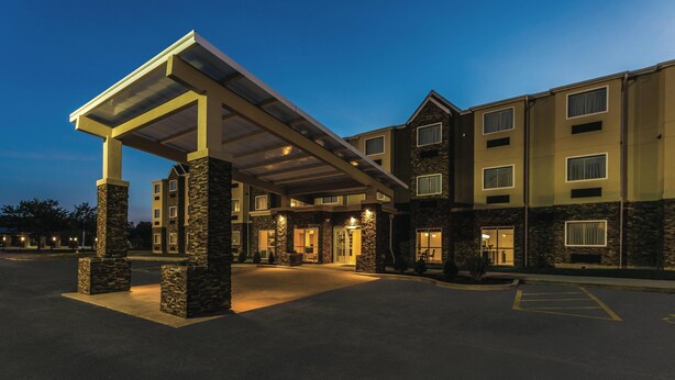 A multi-story hotel with a covered entrance, stone pillars, and a parking lot. - La Quinta Inn & Suites by Wyndham Collinsville - St. Louis (Collinsville)