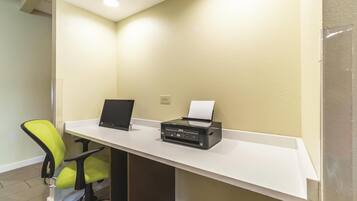 A desk with a laptop and an Epson printer, a green office chair, and a white desk against a textured beige wall.